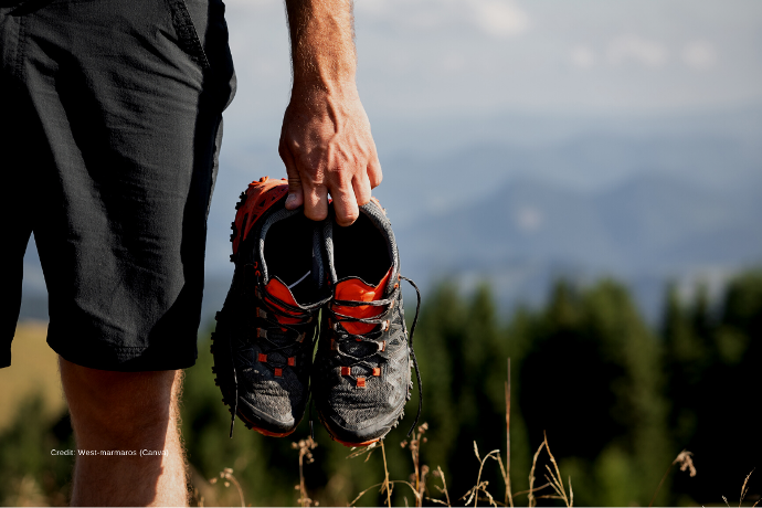 Zu sehen ist ein Mann in Sportbekleidung mit Sportschuhen in der Hand. 